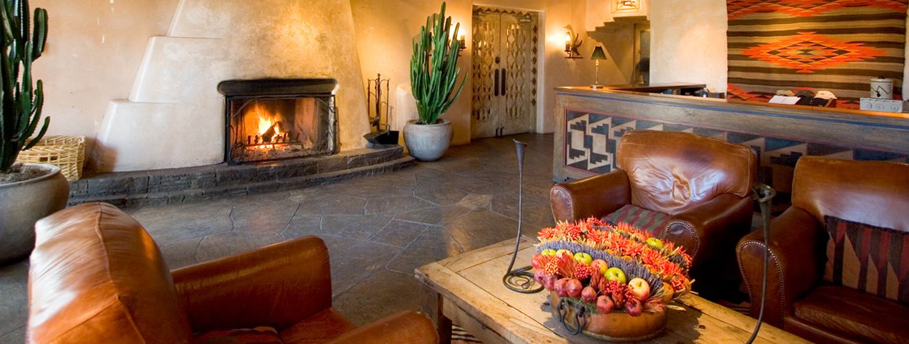 The adobe lobby of the Inn of the Anasazi in Santa Fe — a kiva fireplace, leather chairs and Southwestern textiles aglow in firelight.
