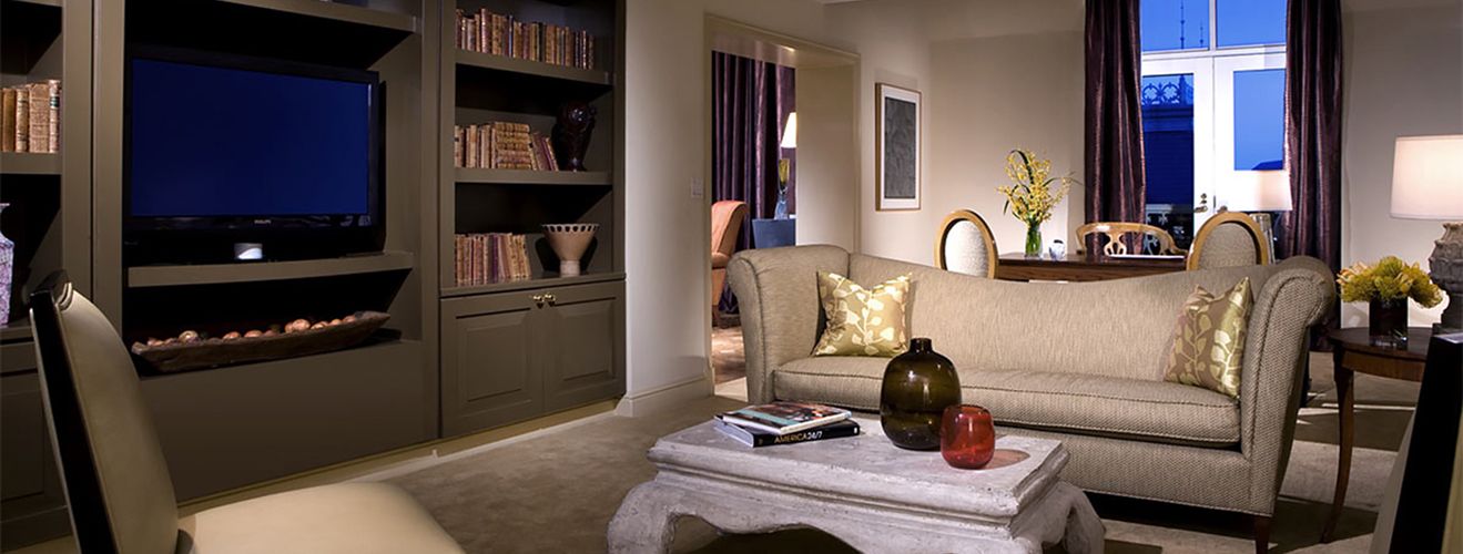 A refined suite at the Hotel Crescent Court in Dallas — a tailored sofa, built-in library and city windows at twilight.