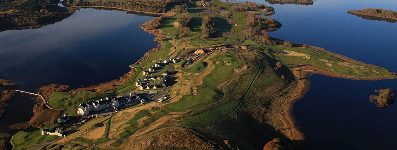 An aerial view of Lough Erne Resort at golden hour — a championship golf course wrapping a wooded peninsula amid mirror-still lakes.