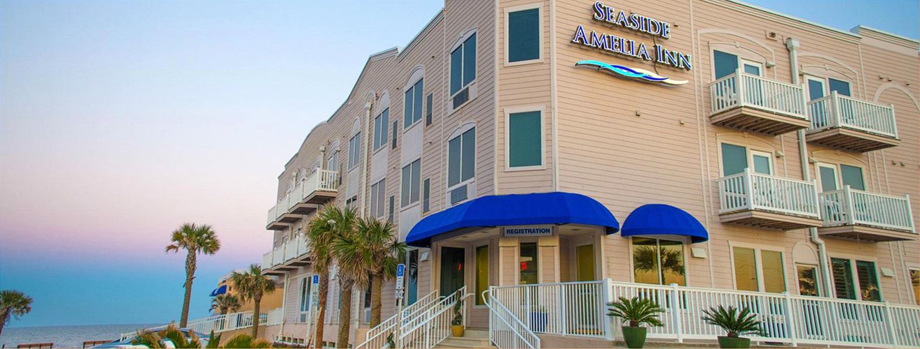 The Seaside Amelia Inn on Amelia Island, Florida — blue awnings and palms beneath a pink-to-blue sunset sky beside the Atlantic.
