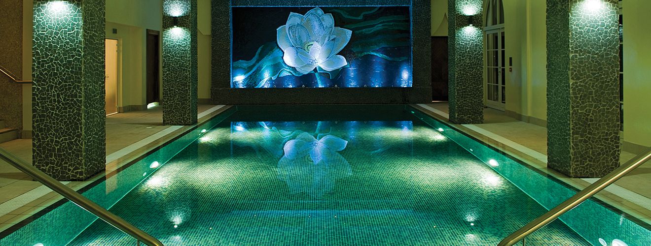 An indoor spa pool lit jewel-teal, a luminous lotus mosaic mirrored on still water.